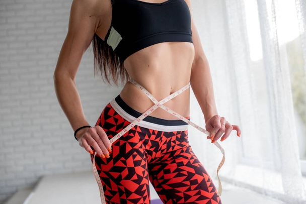 Athletic young girl measures her slender waist. Healthy lifestyle - Foto, imagen