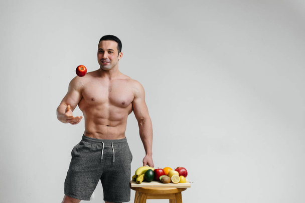 Sportos szexi srác pózol fehér háttérrel fényes gyümölcsökkel. Fogyókúra. Egészséges táplálkozás - Fotó, kép