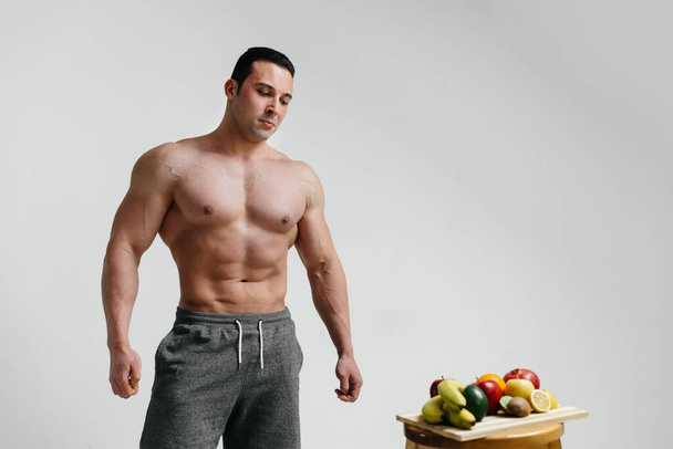 Sexy vegan guy with a naked torso posing in the Studio next to fruit. Diet. Healthy diet - Foto, Imagen