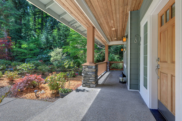 Длинный двухэтажный северо-западный экстерьер дома в серо-зеленом цвете с весенним ландшафтом и большим палисадником с деревянным потолком и видом на лес
. - Фото, изображение
