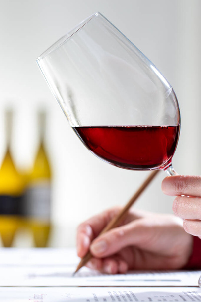 Colpo verticale ravvicinato dell'enologo che valuta corpo e colore del vino rosso a tavola
. - Foto, immagini