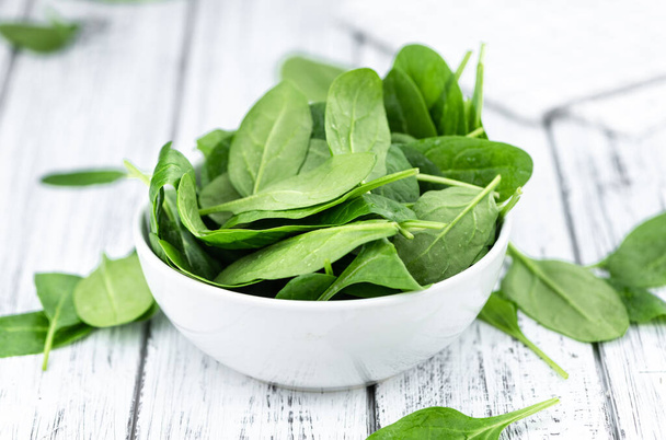 Portion of fresh Spinach on an old wooden table (close-up shot) - 写真・画像