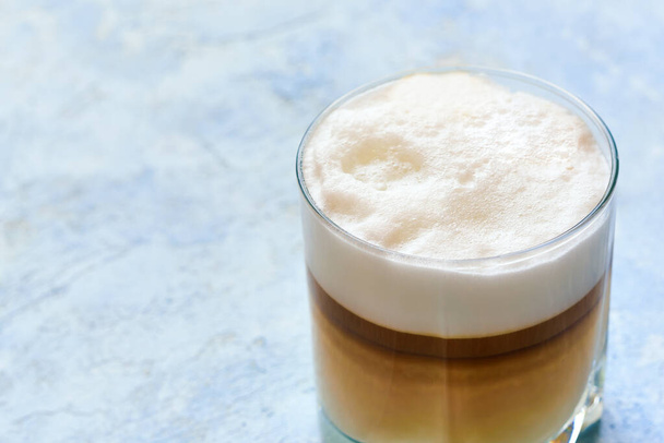 cappuccino in a glass cup prepared in a home coffee machine on a blue background. - 写真・画像
