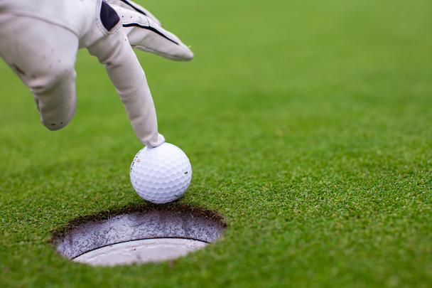 Die Hand eines Mannes, der einen Golfball in ein Loch auf dem grünen Feld wirft - Foto, Bild