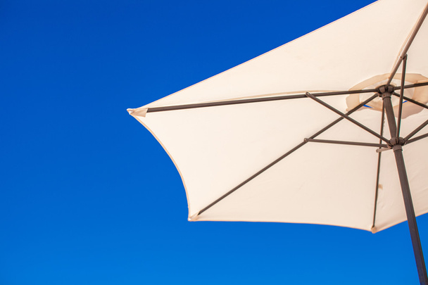 Osa valkoinen sateenvarjo taustalla sininen taivas rannalla
 - Valokuva, kuva