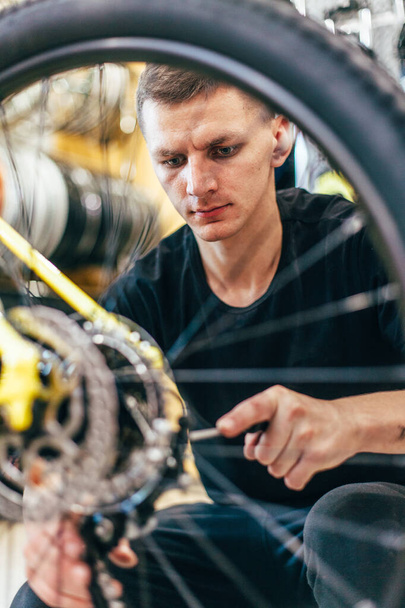 Ο τύπος επισκευάζει ένα ποδήλατο σε ένα εργαστήριο ποδηλάτων. - Φωτογραφία, εικόνα