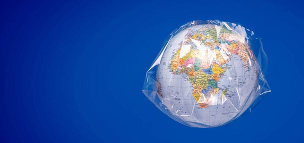 A world globe wrapped in plastic. Plastic contamination or protection against the epidemic infectious diseases or the air pollution. Blue studio background. - Foto, Bild