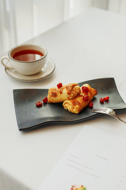 frittelle con ciliegie su un piatto nero e una tazza di tè
 - Foto, immagini