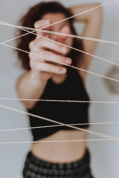 A vertical shot of a female trying to touch white threads hanging in front of her, intersecting with one another - Photo, Image