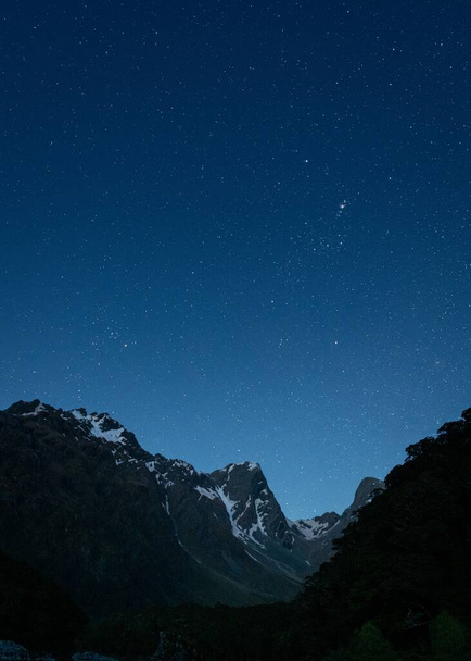 A vertical shot of mountains under a dark blue sky filled with stars - Valokuva, kuva