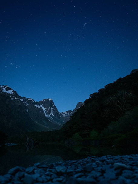 A vertical shot of mountains under a blue star-filled sky - Фото, зображення