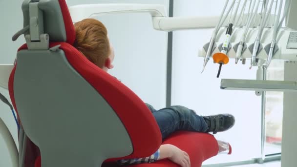 Mały chłopiec w recepcji u dentysty na krześle dentystycznym, który się podnosi. Stomatologia dziecięca - Materiał filmowy, wideo