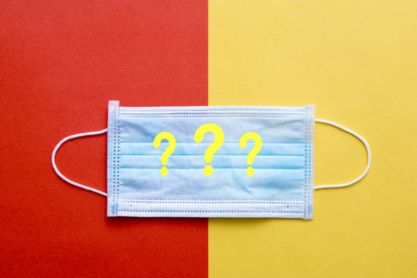 Simple medical mask on a red background with yellow question marks. Creative. Copy space. - Foto, immagini
