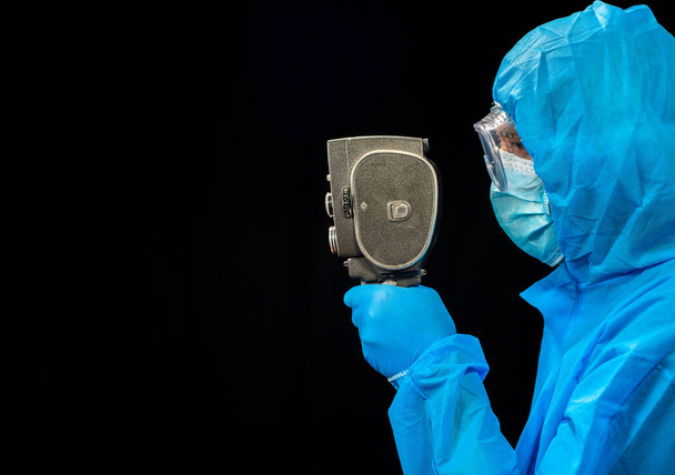 Retro movie camera. A man in a protective antivirus suit holds a retro movie camera in his hand. - Zdjęcie, obraz