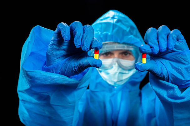Ιός. Μια γυναίκα με προστατευτική στολή κατά του ιού κρατά ένα χάπι για τον ιό στα χέρια της.. - Φωτογραφία, εικόνα