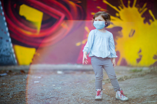 a small, beautiful girl, in a medical mask, stands on the street - Fotografie, Obrázek