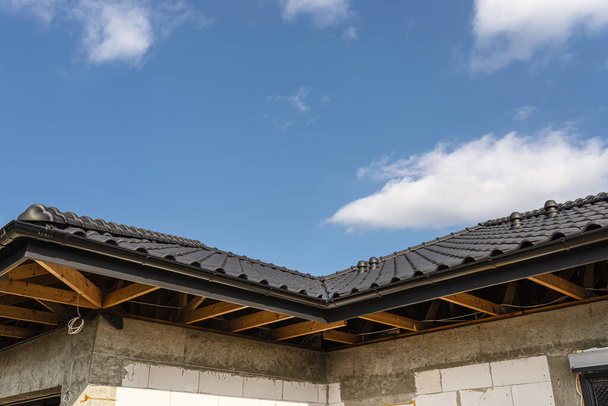 Mavi gökyüzüne karşı antrasit seramik fayansla kaplı tek bir aile evinin çatısı görünür kirişler.. - Fotoğraf, Görsel