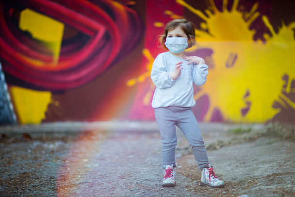 a small, beautiful girl, in a medical mask, stands on the street - Фото, зображення