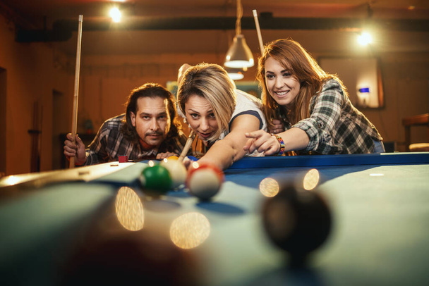 Jóvenes amigos sonrientes y alegres están jugando billar en el bar después del trabajo. Participan en actividades recreativas. - Foto, imagen