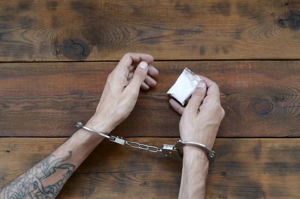 Pidätetty huumediileri kädet poliisin käsiraudoissa pieni heroiini huumeiden paketti tumma puinen pöytä tausta. Laittoman huumekaupan käsite. Huumekauppiaiden kanssa kamppailu
 - Valokuva, kuva