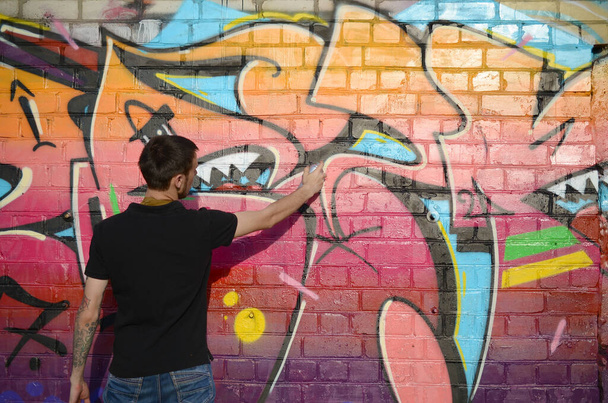 Sırt çantası ve gaz maskesi takan genç grafiti sanatçısı, tuğla duvara pembe tonlarda grafiti yapıyor. Sokak sanatı ve çağdaş boyama süreci. Gençlik alt kültüründe eğlence - Fotoğraf, Görsel