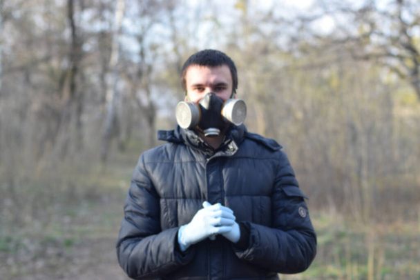 保護ガスマスクの若い男のぼやけた肖像は、春の森の中で屋外ゴム使い捨て手袋を身に着けています。検疫中の保護用品の使用の概念 - 写真・画像