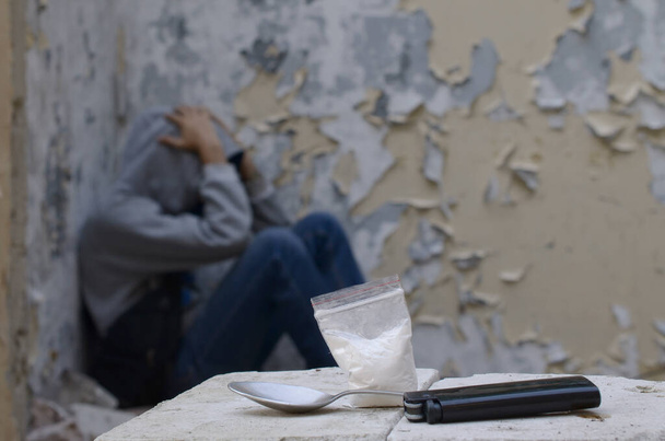 Un hombre drogadicto sufre de abstinencia mientras está sentado en un edificio abandonado junto a una dosis para inyectables de narcóticos. Concepto de problemas de drogadicción
 - Foto, Imagen
