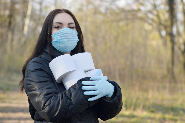 Covidiot-Konzept. Junge Frau in Schutzmaske hält viele Rollen Toilettenpapier im Freien im Frühlingsholz. Panikkauf während der Quarantäne - Foto, Bild