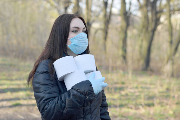 Covidiot-Konzept. Junge Frau in Schutzmaske hält viele Rollen Toilettenpapier im Freien im Frühlingsholz. Panikkauf während der Quarantäne - Foto, Bild