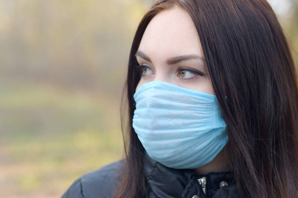 Portret van jonge brunette vrouw in blauw beschermend masker buiten in lentehout. Begrip gebruik van beschermende goederen tijdens quarantaine - Foto, afbeelding