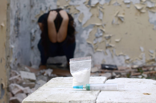 薬物依存の女性は、麻薬注射のために放棄された建物と汚い注射器に座っている間、薬物離脱に苦しんでいます.薬物中毒問題の概念 - 写真・画像