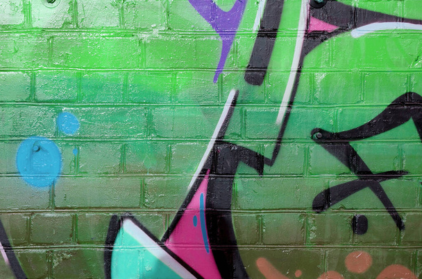 Abstract colorful fragment of graffiti paintings on old brick wall in green colors. Street art composition with parts of unwritten letters and multicolored stains. Subcultural background texture - Photo, Image