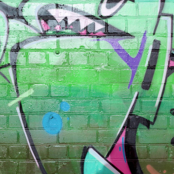 Abstrakcyjny kolorowy fragment malowideł graffiti na starej ceglanej ścianie w zielonych kolorach. Uliczna kompozycja sztuki z częściami niepisanych listów i wielokolorowymi plamami. Tekstura tła subkulturowego - Zdjęcie, obraz