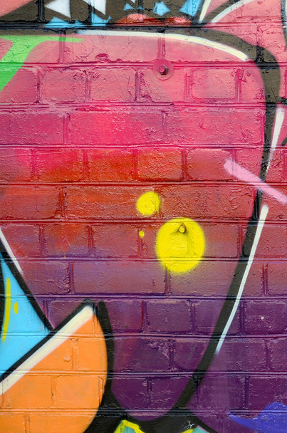 Абстрактный красочный фрагмент граффити на старой кирпичной стене. Уличная художественная композиция с неписаными буквами и разноцветными пятнами. Субкультурная текстура фона в красных цветах
 - Фото, изображение