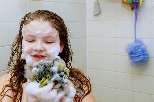 Милая маленькая девочка купается в пенной ванне, моет голову.
 - Фото, изображение