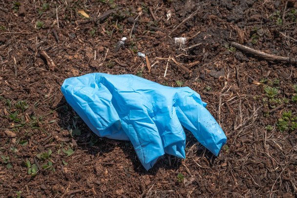 Een gebruikte afgedankte blauwe latex handschoen ligt op een mulch in een parkway met de vingers binnenstebuiten tijdens de COVID-19 coronavirus uitbraak en pandemie. - Foto, afbeelding
