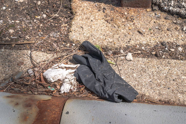 Použitá odhozená černá latexová rukavice leží na některých kamenech v parkway s prsty naruby během vypuknutí koronaviru COVID-19 a pandemie. - Fotografie, Obrázek