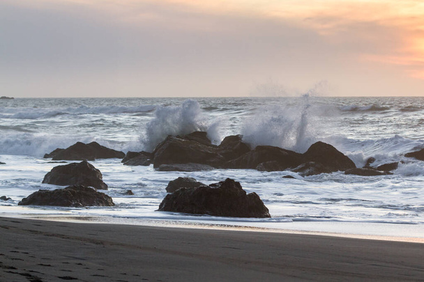 Rocky partvonal Nesika Beach, Oregon késő délután a nap közeledik a horizont és a hullámok ütköznek a sziklák - Fotó, kép