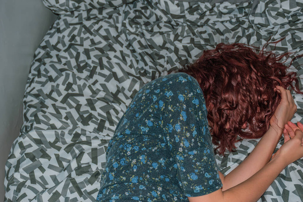 Egy közeli kép, amin egy felismerhetetlen, fiatal, kaukázusi vörös hajú nő fekszik az ágyon az oldalán. - Fotó, kép