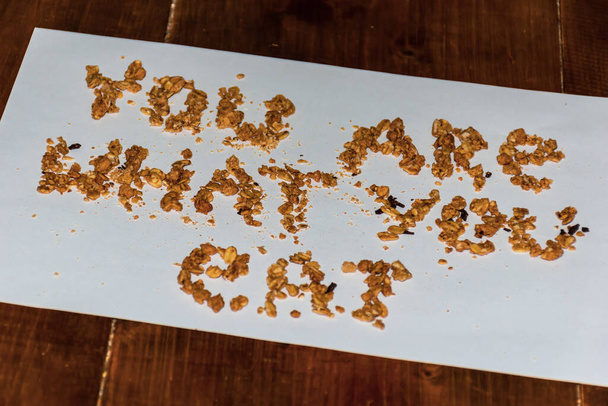 A close-up shot of cereal grains spelling the saying 'You are what you eat' on a paper sheet lying on a wooden table - Photo, image