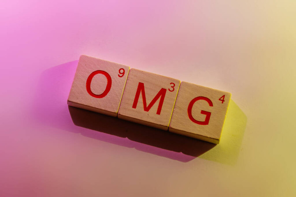 Un gros plan de tuiles carrées en bois orthographiant le mot "omg" illuminé par un rose / magenta doux et vibrant et une lumière jaune / dorée des côtés opposés
 - Photo, image