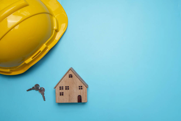 шолом з дерев'яним будинком і ключем на синьому фоні, концепція нерухомості
 - Фото, зображення