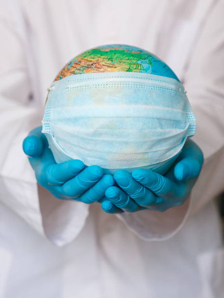 globe with a medical mask from covid-19 virus in hands ofdoctor close-up. concept epidemic and pandemic of Coronavirus. - Photo, Image