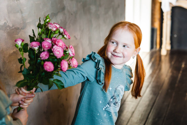 Ein kleines Mädchen mit roten Haaren nimmt Schwester die Blumen weg, Pflanzen, Kinder kämpfen, Spielzeug und Dinge, Streitigkeiten, Eltern sind aufgebracht, versöhnen Kinder, Familienbeziehungen, Liebe, Gefühle, Kindheit - Foto, Bild