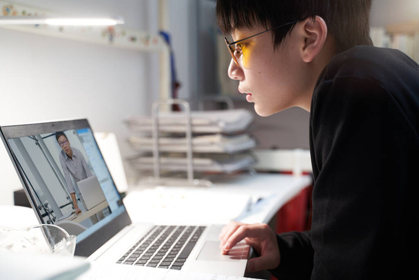アジアの子供勉強ホーム上のラップトップ身に着けていますコンピュータ眼鏡の間にcovid-19 - 写真・画像