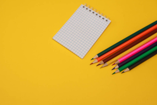 Colored pencils and a white sheet of notepad on a yellow background, space for text. Flat lay. - Fotó, kép