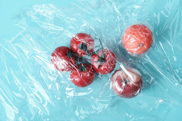 Recycling and environment concept: fresh red tomato apple and orange in plastic package. Vegetables wrapped in plastic cellophane in green background - Fotoğraf, Görsel