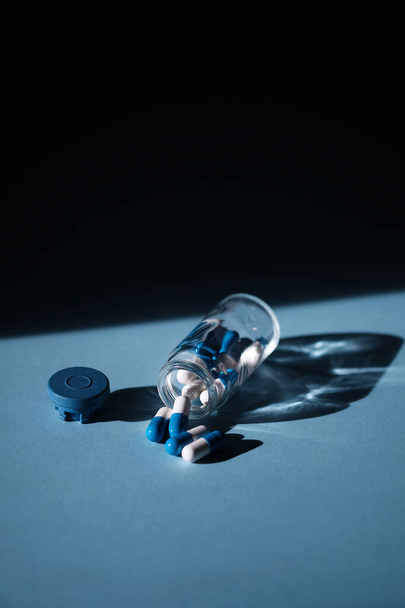 Open glass bottle with scattered antibiotic pills or tablets on a blue table background with emty copy space - Foto, Imagem