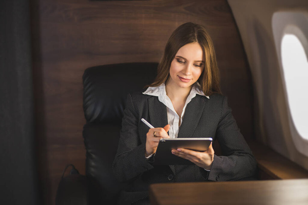 Attractive caucasian businesswoman sitting in comfortable seat in airplane, holding modern tablet, working using wireless connection on board. Business, traveling and technology. - Foto, immagini
