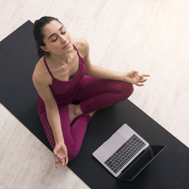 COVID-19 autoisolamento. Latina ragazza prendendo yoga tutorial sul computer portatile, facendo esercizi di respirazione o meditazione, sopra vista
 - Foto, immagini